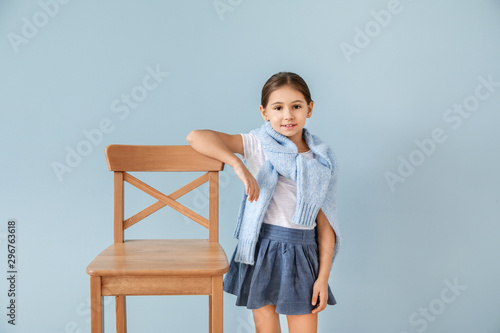 Cute fashionable girl with chair on color background