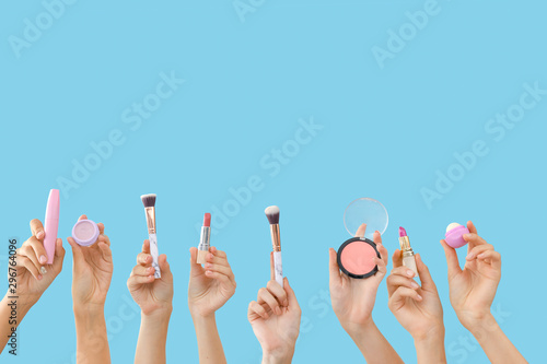 Many hands with decorative cosmetics and makeup brushes on color background
