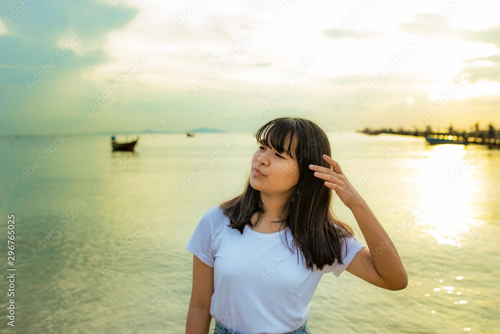 cheerful asian teenager standing at seaside against beautiful sunset sky