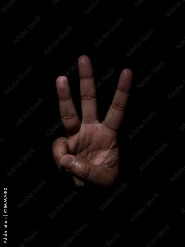 Low key photo of a brown man showing the number three with his fingers on a plain black background