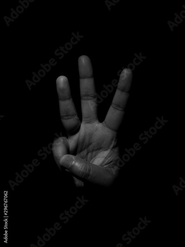 Low key black and white photo of a man showing the number three with his fingers on a plain black background