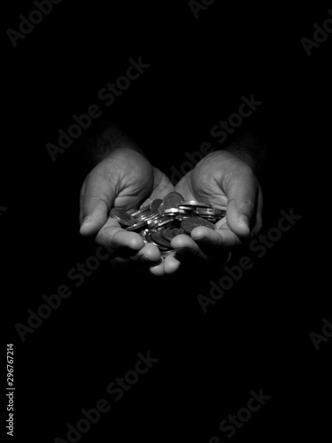 Low key black and white photo of a man holding several coins in his hands.