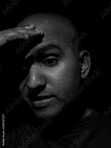 Low key black and white closeup photo of a bald man placing hand on forehead due to headache