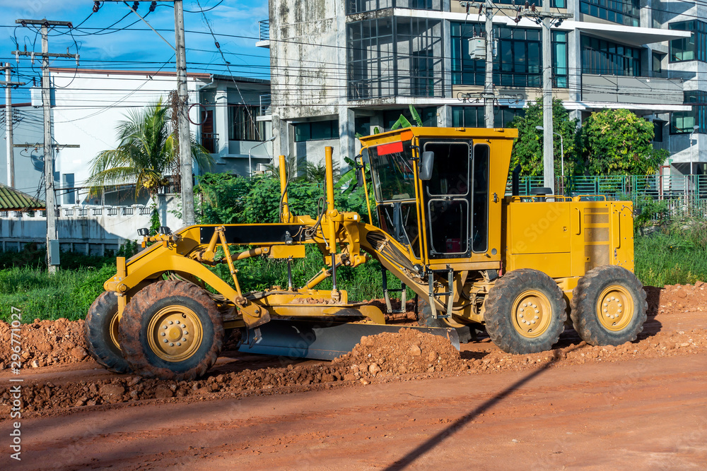 The motorgrader  is working in the land site with red soil land and buildings in the sun of afternoon. 
