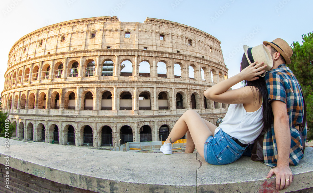 Lovely couple of tourist sitting on a wall at Colosseum hugging. Rome, Italy