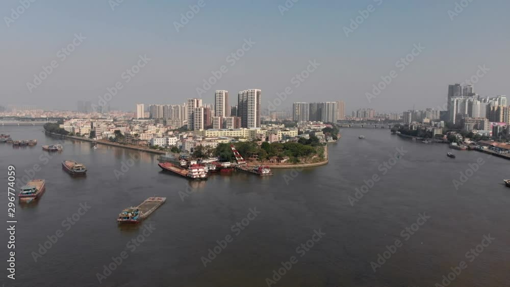 The navigable river diverges into two streams in the middle of a large residential area. In the frame, a large number of cargo ships are anchored. Very dirty water in the river. Guangzhou, China The navigable river diverges into two streams in the middle of a large residential area. In the frame, a large number of cargo ships are anchored. Very dirty water in the river. Guangzhou, China