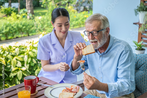 Nurse assist elderly senior man to eat breakfast at nursing home