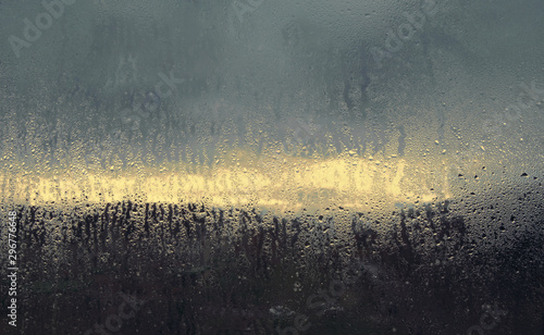 A window with fogged glass. Autumn rainy morning landscape is seen - a bright strip between heavy blue clouds.