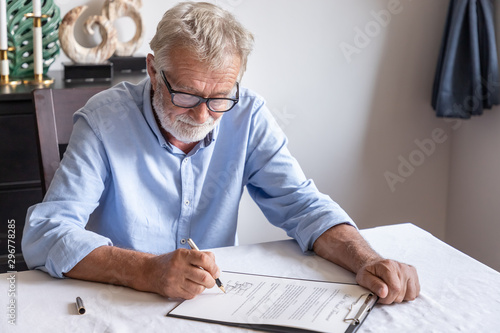 Senior old man elderly examining and signing last will and testament; document is mock-up.