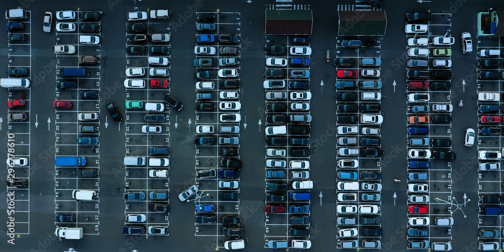 Aerial shot of crowded parking with many cars near the supermarket. View from above. Many cars are parked on an asphalt parking area with white markings.