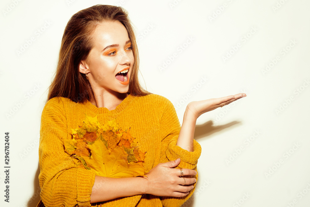 Beautiful brunette with long hair shows her hand at the text. A girl in a yellow sweater holds autumn leaves, rejoices, has fun, and is surprised. Empty seat, girl holds a product. Autumn discounts. Beautiful brunette with long hair shows her hand at the text. A girl in a yellow sweater holds autumn leaves, rejoices, has fun, and is surprised. Empty seat, girl holds a product. Autumn discounts.