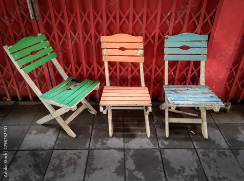 Green  orange and blue old wooden vintage chairs with red metal facade in the background