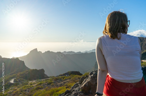 Blond woman sitting with contemplation, enjoying the moment on the sunset in the mountain, relaxing and dreaming. Adolescent girl looking to the horizon alone with casual clothes from the back