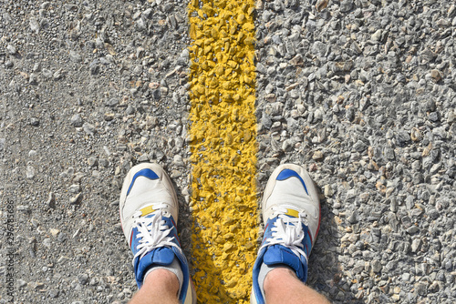 man stands on the asphalt road between the dividing line in white sneakers close-up