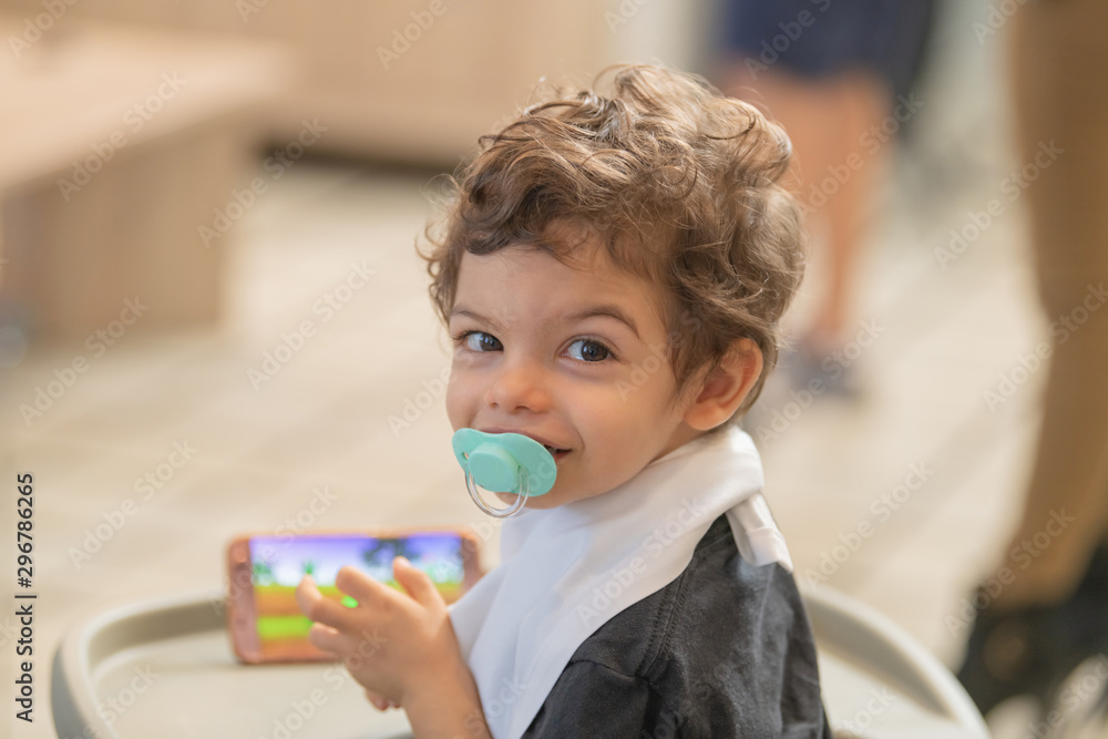 Portrait of a beautiful child with brown hair and a pacifier in the mouth, with the background out of focus. Concept of innocence and child tranquillity. Portrait of a beautiful child with brown hair and a pacifier in the mouth, with the background out of focus. Concept of innocence and child tranquillity.