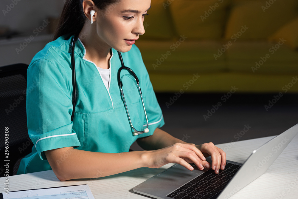 attractive nurse in uniform sitting at table and using laptop during night shift attractive nurse in uniform sitting at table and using laptop during night shift