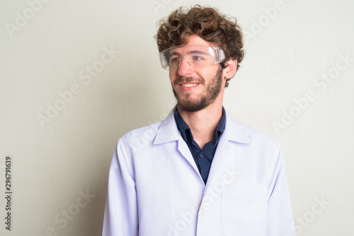 Face of happy young bearded man doctor as scientist with protective glasses thinking