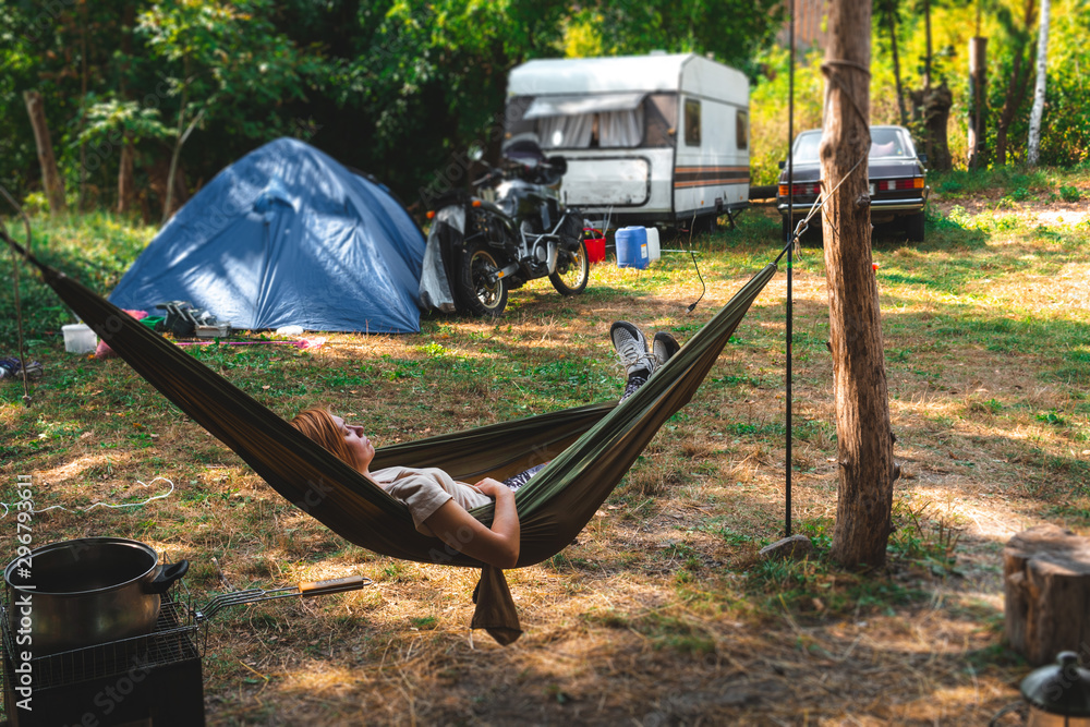 Girl resting in a hammock. Day time camp in the forest, trailer house and  touristic tent. adventure motorcycle tour, seasonal vacation. Stock Photo |  Adobe Stock
