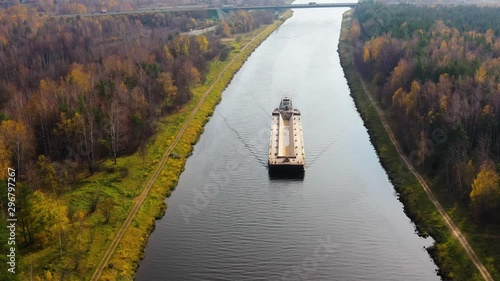River tug with a barge view from above. River channel for freight transportation, top view. Beautiful landscape with a wide river and autumn forest.