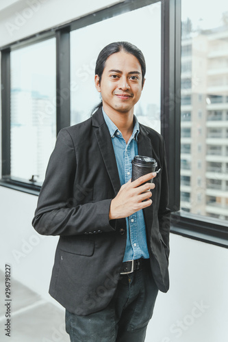 Portrait of handsome young businessman with long dark hair looking away while standing near the window