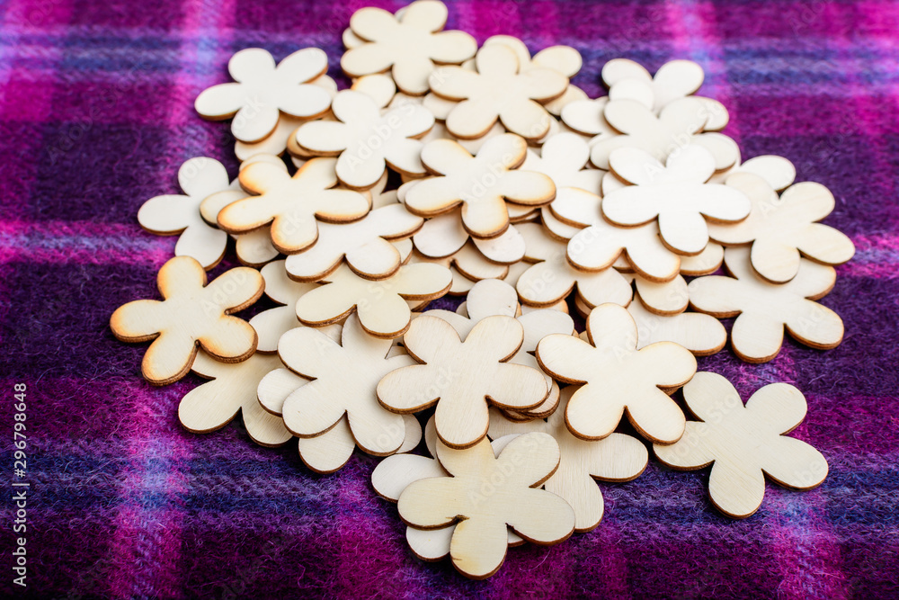 Large group pf delicate light brown wooden flowers on dark mauve textile material background, displayed centred, top view or flat lay with laser cut wooden objects Large group pf delicate light brown wooden flowers on dark mauve textile material background, displayed centred, top view or flat lay with laser cut wooden objects