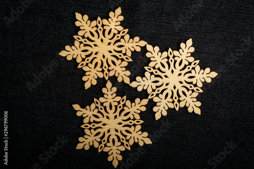 Three delicate light brown wooden snowflake on black textile material background, displayed on centre, top view with space for text around, flat lay with laser cut wooden object
