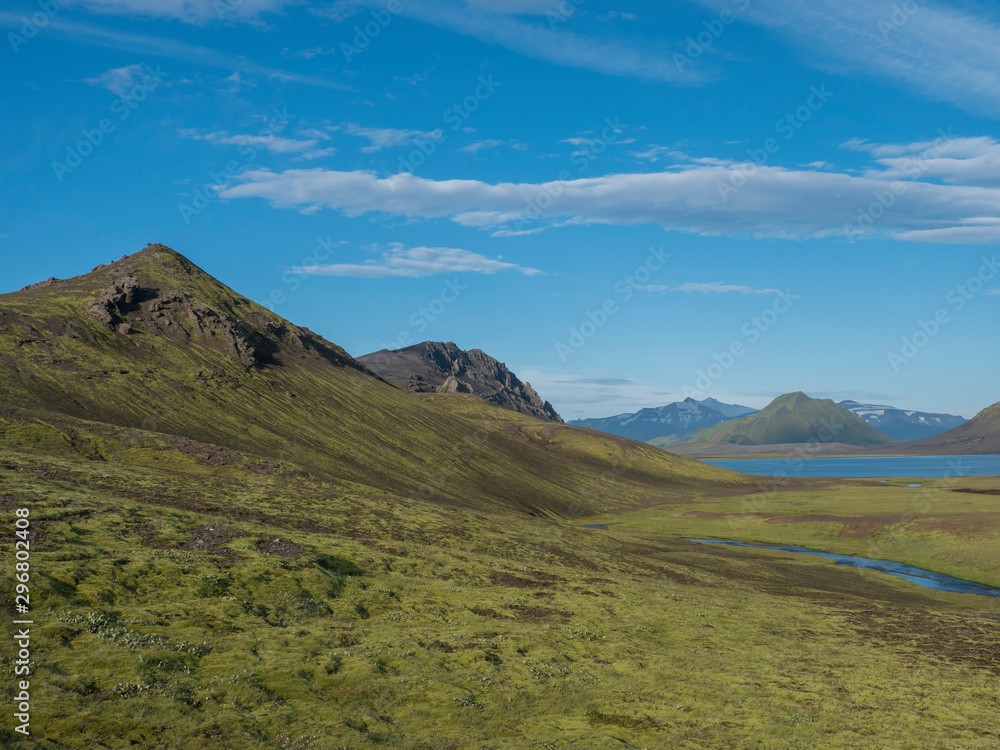 Beautiful landscape of blue Alftavatn lake and river with snow covered mountains and green hills and blue sky background. Summer landscape of the Fjallabak Nature Reserve in the Highlands of Iceland