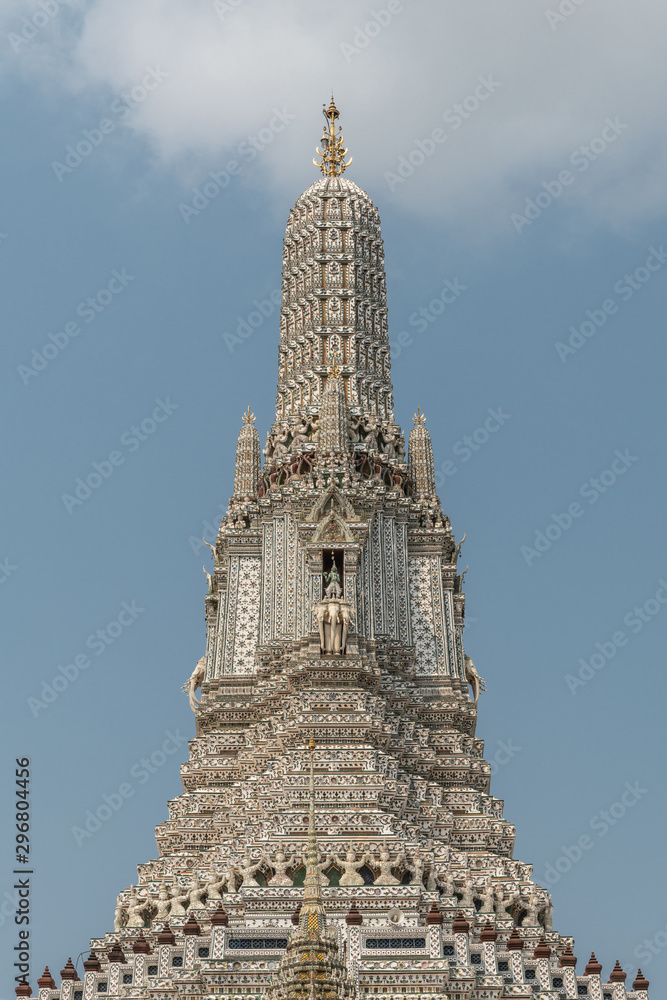 Bangkok city, Thailand - March 17, 2019: Main spire or Prang of Temple of Dawn against blue sky with some white clouds. Porcelain and faience decoration all the way. Hindu Indra riding on Erawan statu