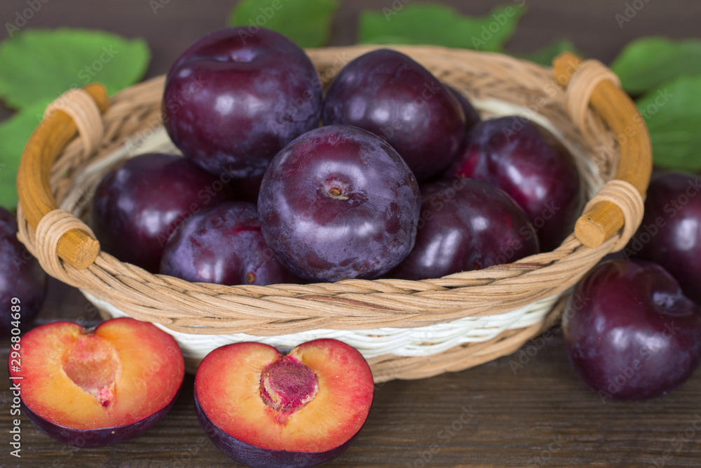 ripe purple plums in a wicker basket close-up. background with whole plums and half plums macro. harvest purple plums. ripe purple plums in a wicker basket close-up. background with whole plums and half plums macro. harvest purple plums.