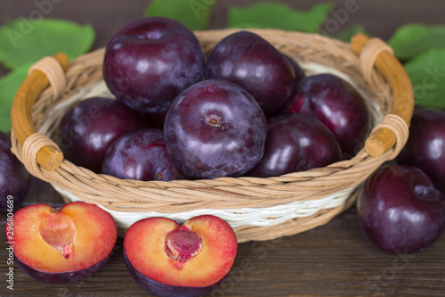 ripe purple plums in a wicker basket close-up. background with whole plums and half plums macro. harvest purple plums.