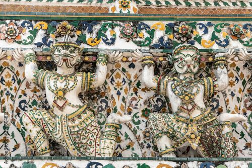 Bangkok city, Thailand - March 17, 2019: Closeup of detail of flank of Temple of Dawn, with its porcelain faience surface, shows two statues of humans pretending to hold up the rest of the temple.