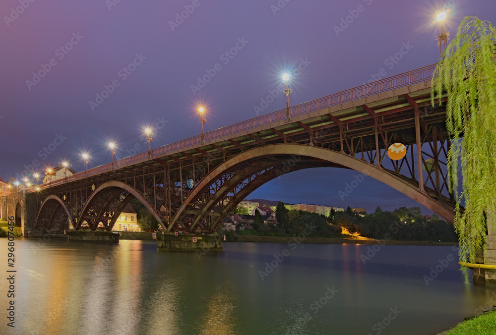 Obraz premium Scenic morning view of illuminated Old Bridge (also named the State) over Drava River. Selective focus with wide angle lens. Concept of landscape and nature. Lower Styria, Maribor, Slovenia