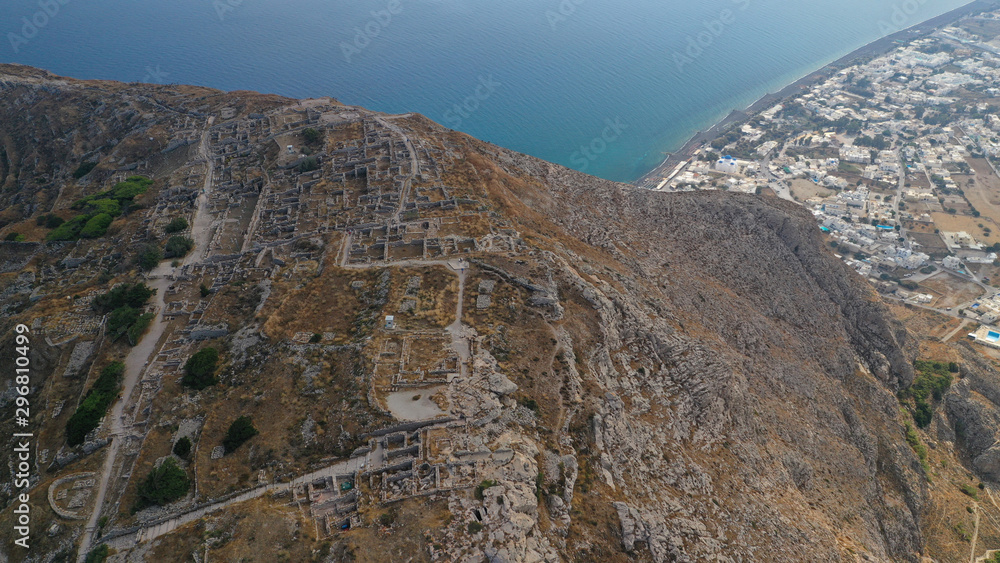 Naklejka premium Aerial drone photo of iconic archaeological site of ancient Thera or Thira built uphill with amazing views to Kamari and Perissa beaches and seaside villages, Santorini island, Cyclades, Greece