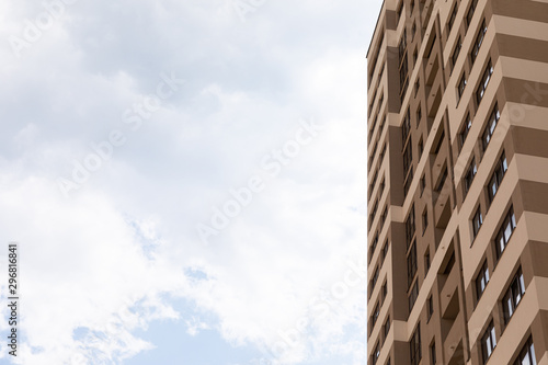 Blue cloudy sky background on one side of photo and high apartment building with beige walls on the right, exterior architecture design