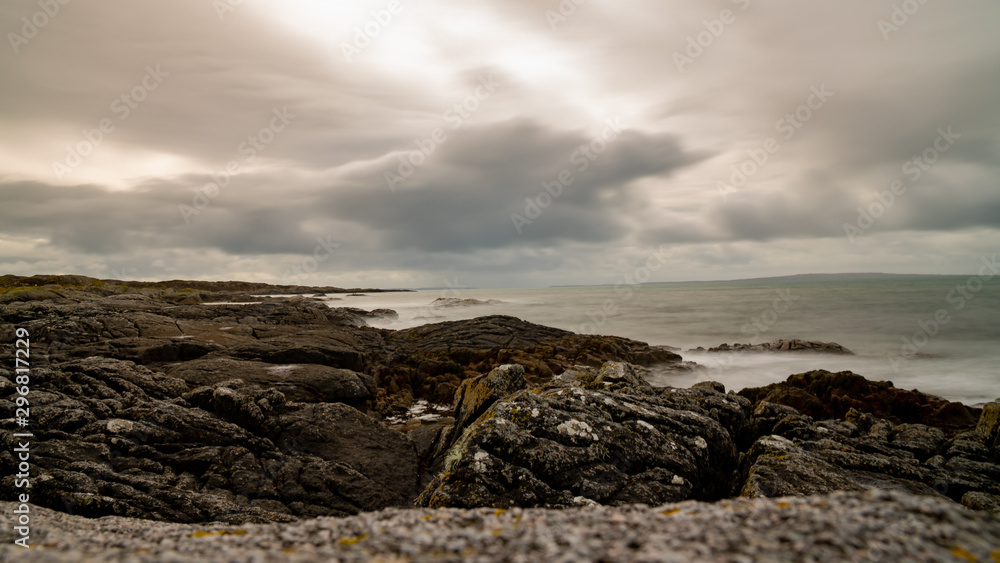 Cloudy sky above rocks, silky smooth water and sharp stones, part of Wild Atlantic Way in Ireland. West Coast