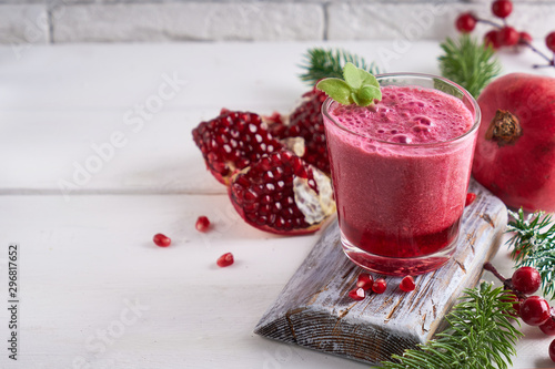 Fotografija pomegranate smoothie in a glass on a white wooden table with fir branches and wi