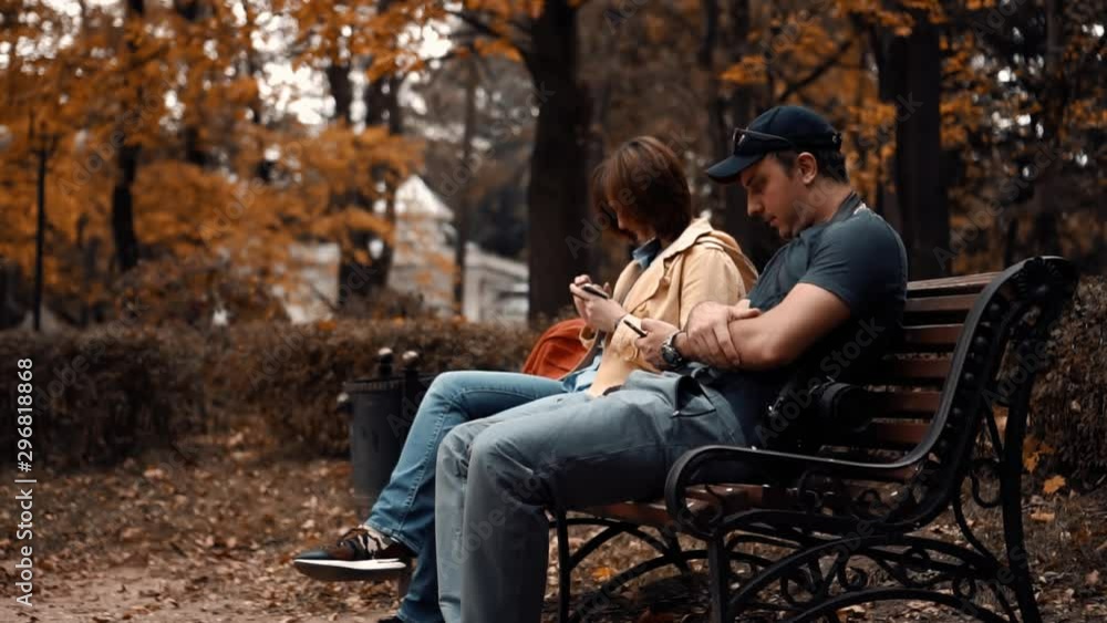 guy and girl are sitting in the park and using phones. quarrel guy and girl are sitting in the park and using phones. quarrel