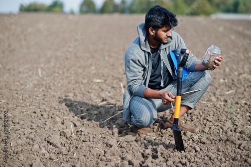 South asian agronomist farmer with shovel inspecting black soil. Agriculture production concept.