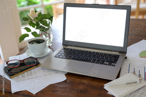 Mockup, laptop with blank white screen on a wooden desk with papers, glasses and a coffee cup, business workspace in a home office, copy space