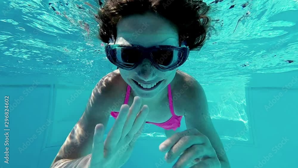 Smiling little girl in swim goggles swimming underwater in pool ...