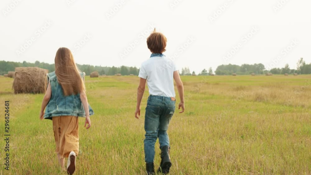 Teenager boy and girl walking on harvesting field on haystack background. Rear view young boy and girl walking on countryside field Teenager boy and girl walking on harvesting field on haystack background. Rear view young boy and girl walking on countryside field