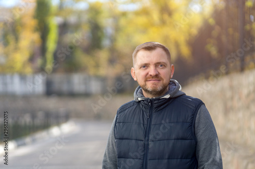 Portrait of a middle-aged man with a beard against the backdrop of an autumn city street.