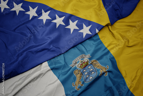 waving colorful flag of canary islands and national flag of bosnia and herzegovina.
