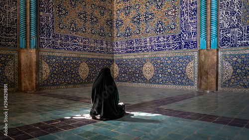 Unidentified Iranian woman wearing chador praying inside Sheikh Lotfollah Mosque with tiles on walls, Isfahan, Iran photo