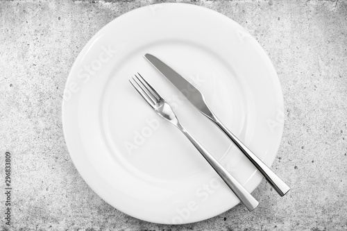 Table setting. Empty plate  knife and fork on a light concrete background. The fork and knife lie in parallel on a plate  the meal is over. Top view and flat lay with copy space.