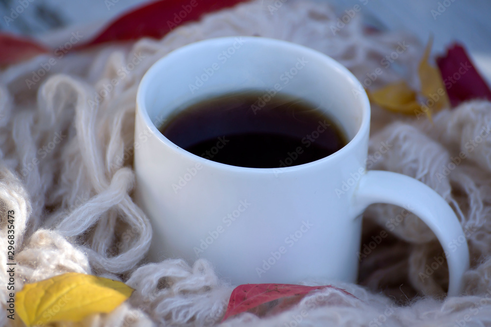 Obraz premium A cup of hot coffee and a warm knitted scarf and bright leaves.