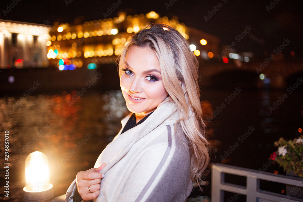 Stylish and elegant young woman in a beige coat on the city waterfront.