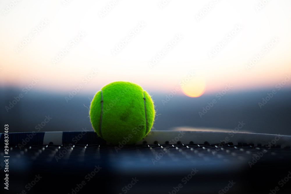 Close-up of tennis ball on net of racket at sunset.