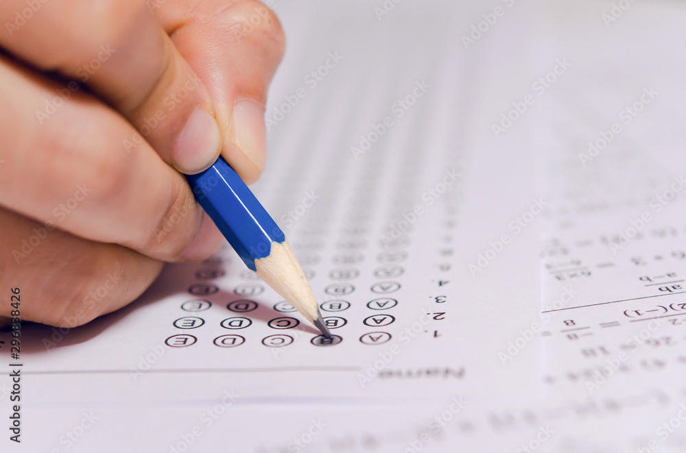 Students hand holding pencil writing selected choice on answer sheets and Mathematics question sheets. students testing doing examination. school exam Students hand holding pencil writing selected choice on answer sheets and Mathematics question sheets. students testing doing examination. school exam