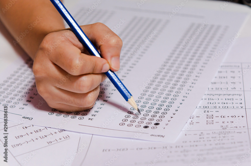 Students hand holding pencil writing selected choice on answer sheets and Mathematics question sheets. students testing doing examination. school exam Students hand holding pencil writing selected choice on answer sheets and Mathematics question sheets. students testing doing examination. school exam